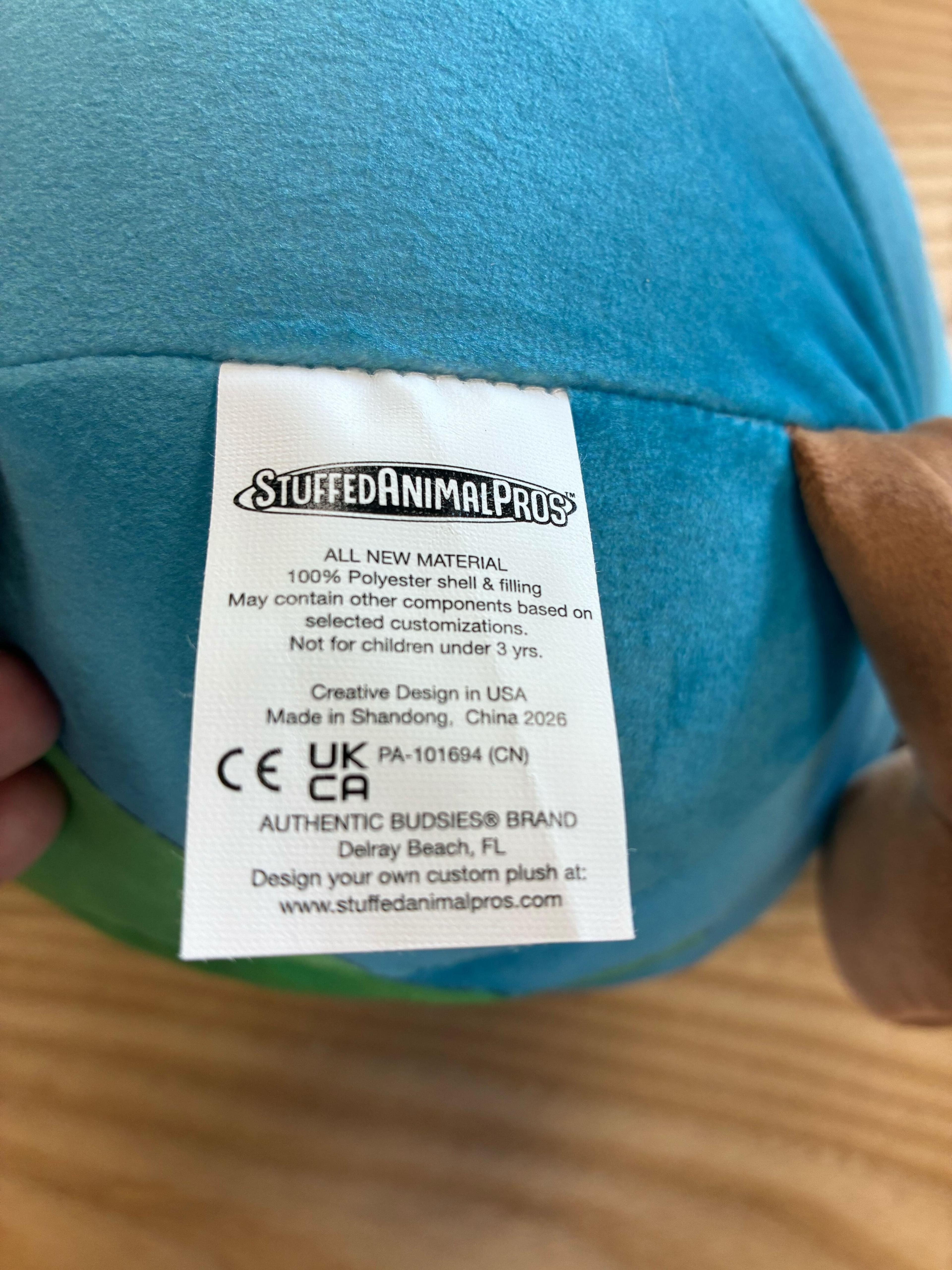 Blue plush toy tag showing Stuffed Animal Pros brand, 100% polyester, made in China