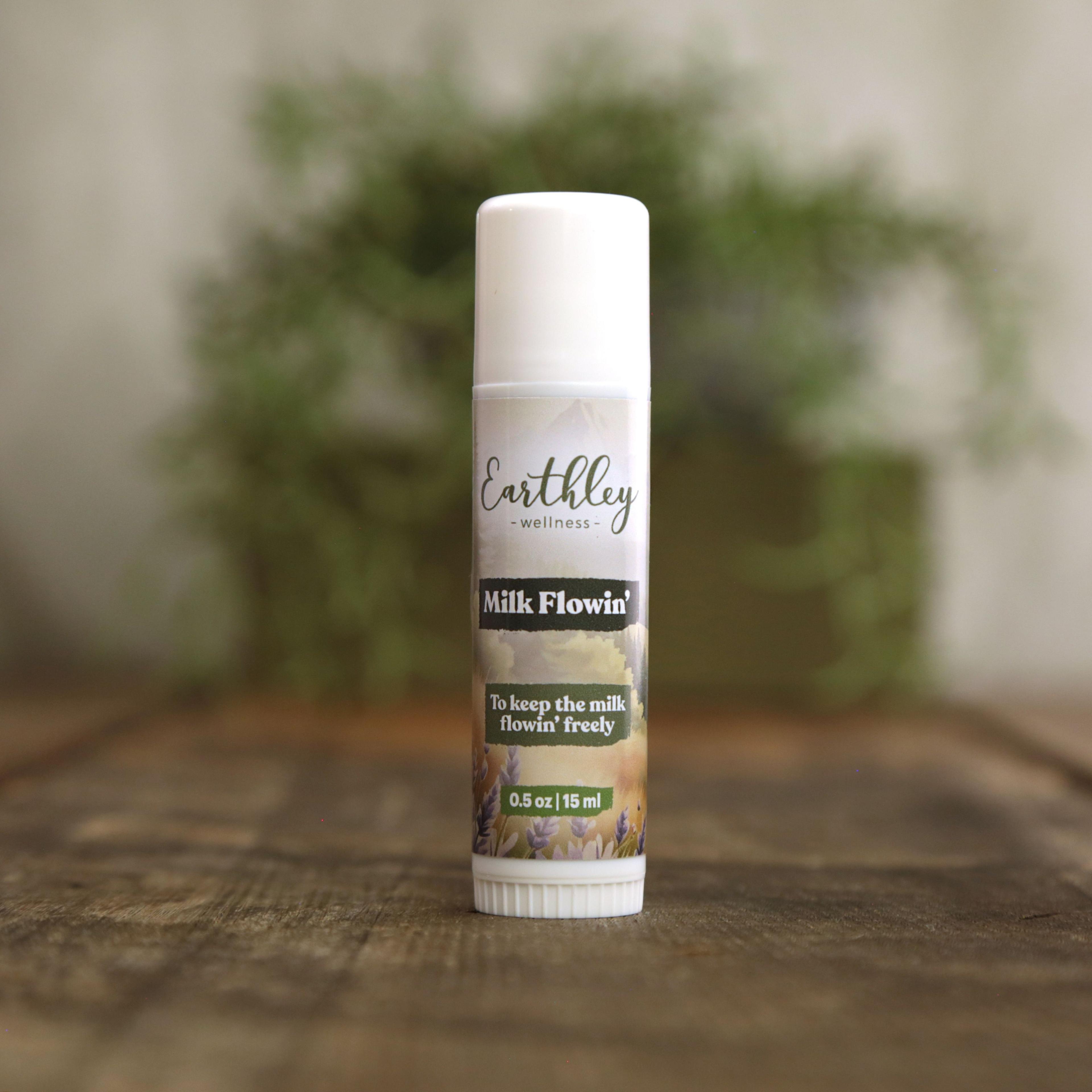 Earthley Milk Flowin 0.5 oz white lip balm style tube with botanical label featuring lavender and meadow landscape, with tagline To keep the milk flowin freely, on wooden surface with greenery in background