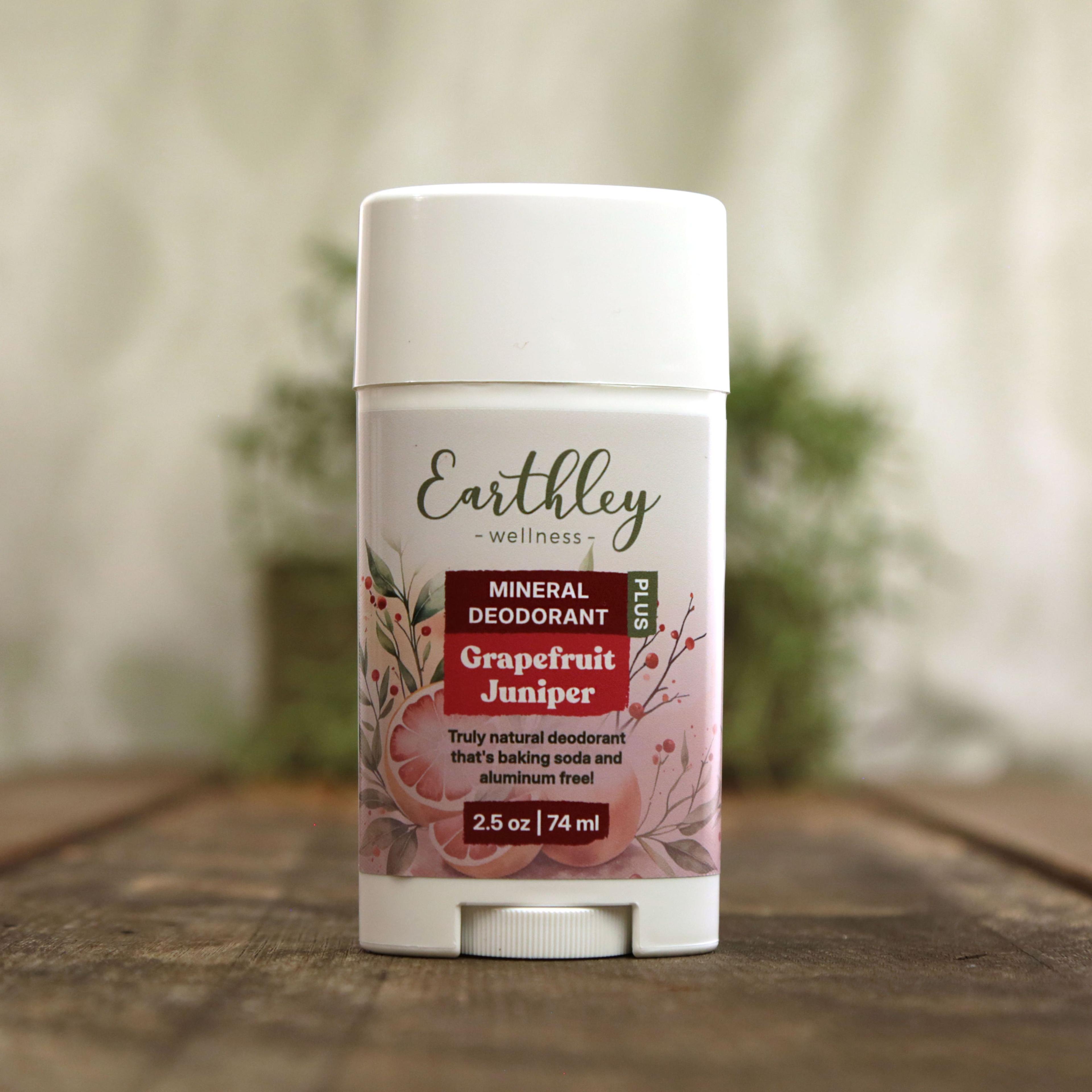 Earthley Mineral Deodorant Plus Grapefruit Juniper 2.5 oz white twist-up stick with botanical label featuring pink grapefruit slices and red berries, labeled as truly natural baking soda and aluminum free deodorant, on wooden surface with greenery in background