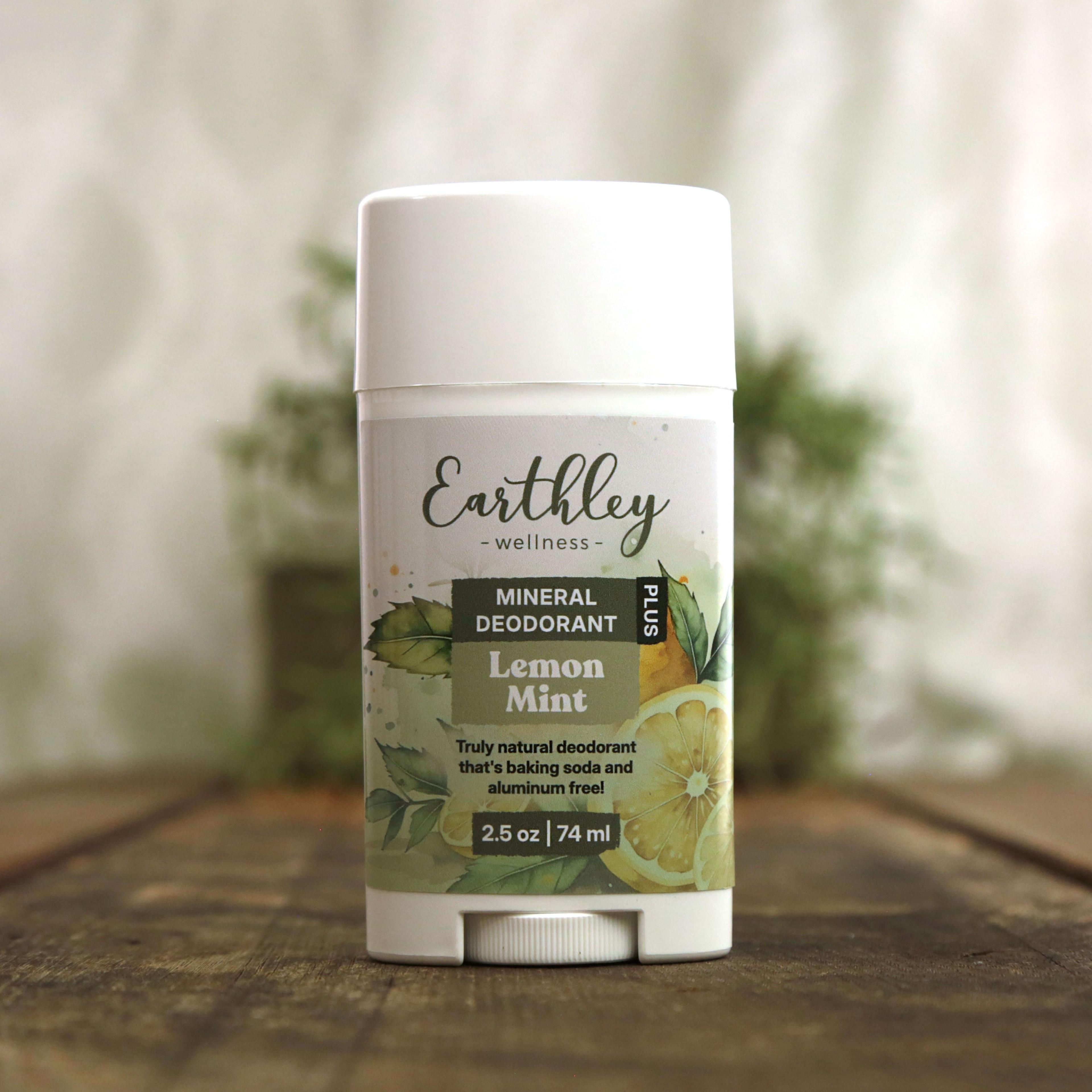 Earthley Mineral Deodorant Plus Lemon Mint 2.5 oz white twist-up stick with botanical label featuring lemon slices and green mint leaves, labeled as truly natural baking soda and aluminum free deodorant, on wooden surface with greenery in background