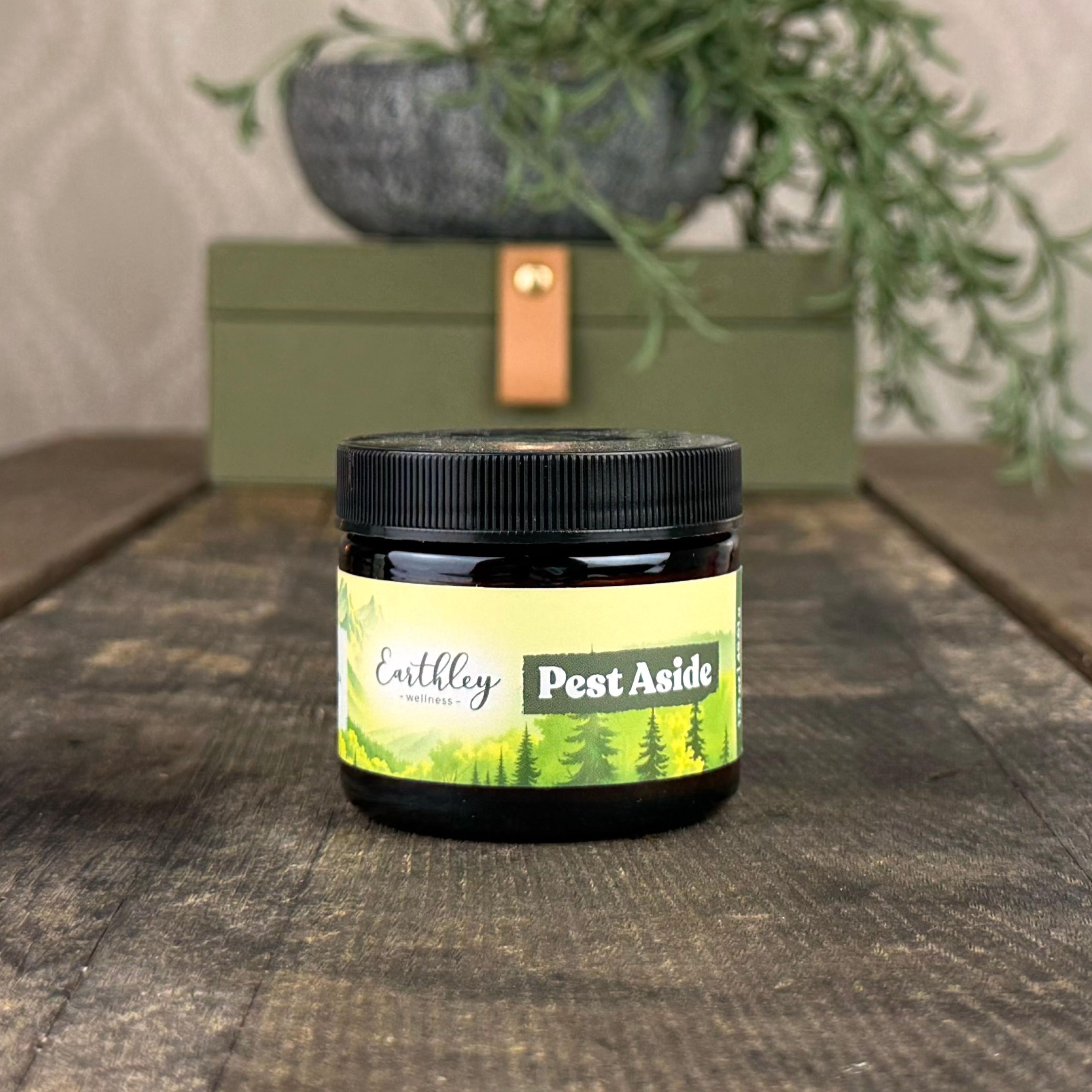 Earthley Wellness Pest Aside salve in amber jar with forest-themed label on wood surface