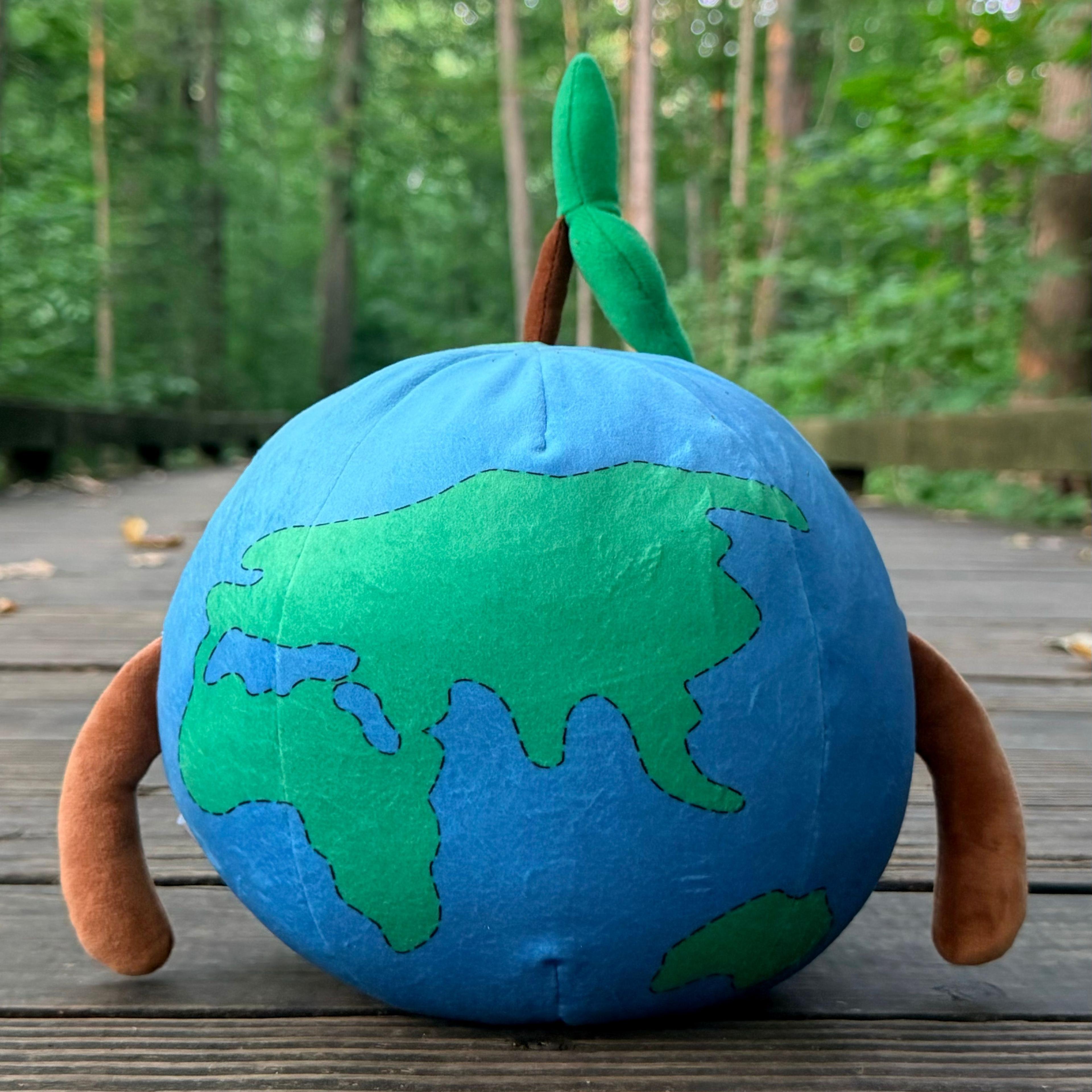 Earthley plush globe toy with green continents, arms, and sprout, on wooden deck