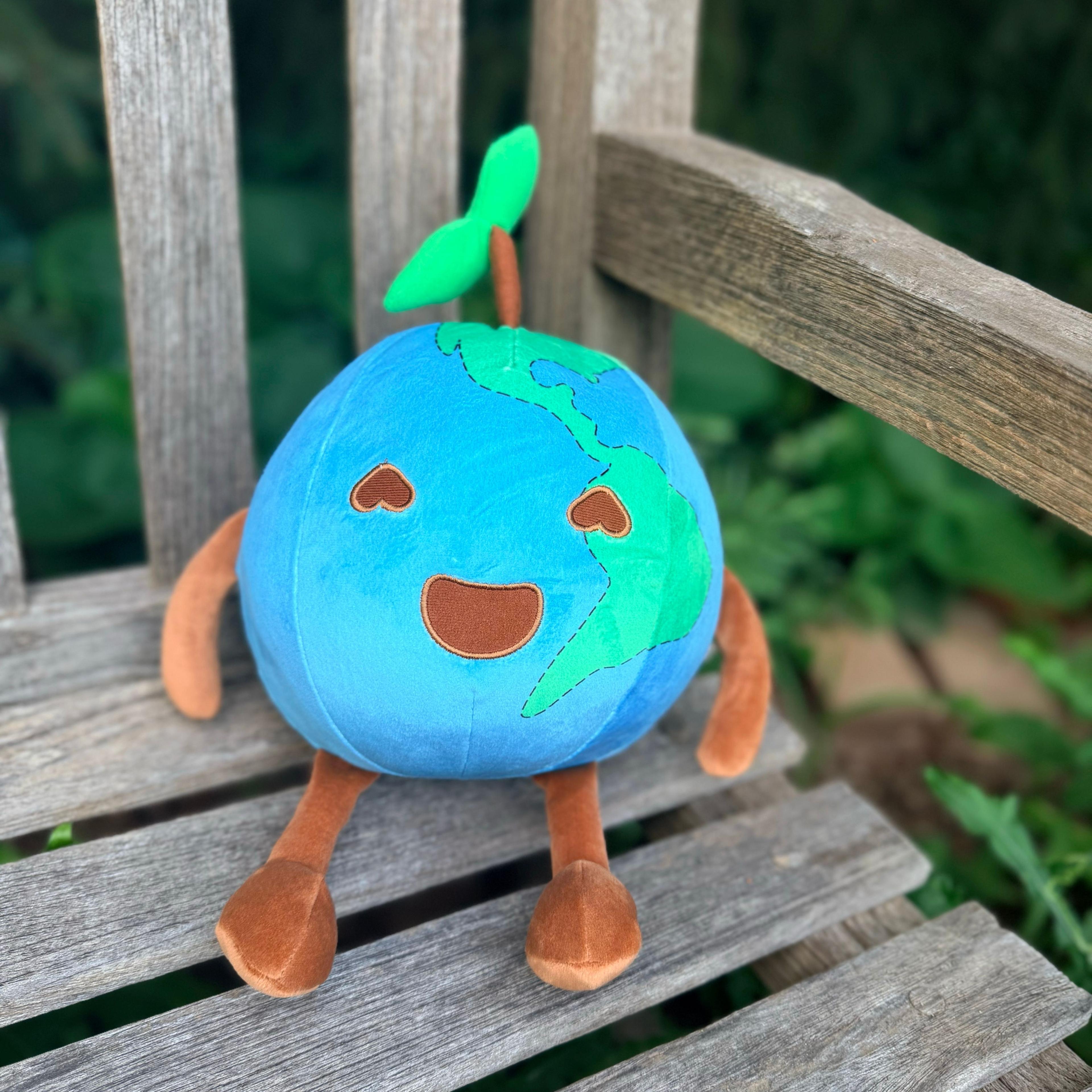 Smiling Earth plush toy with green sprout, heart eyes, and brown limbs on wooden bench