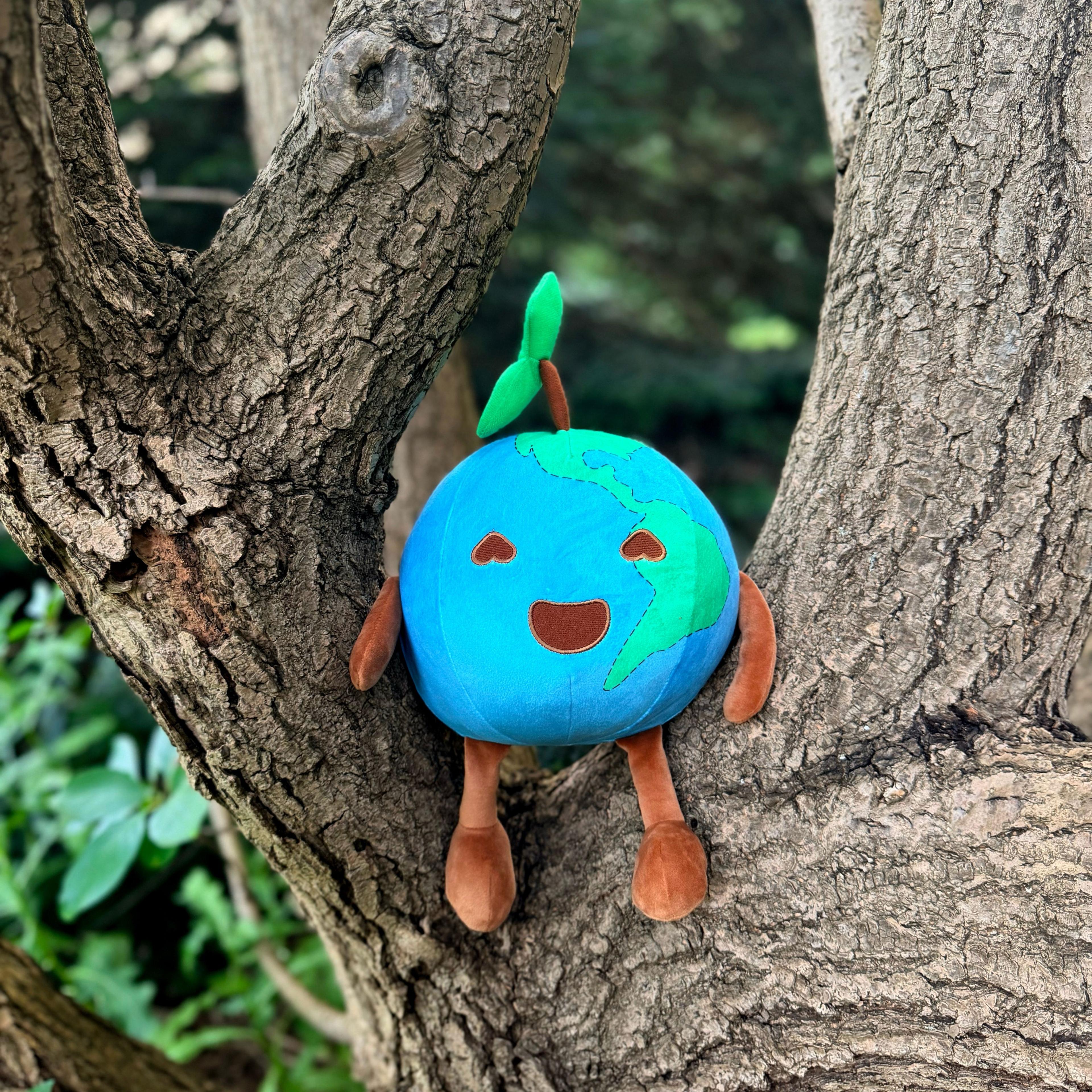 Smiling Earth plush toy with heart eyes and green sprout, nestled in tree branches