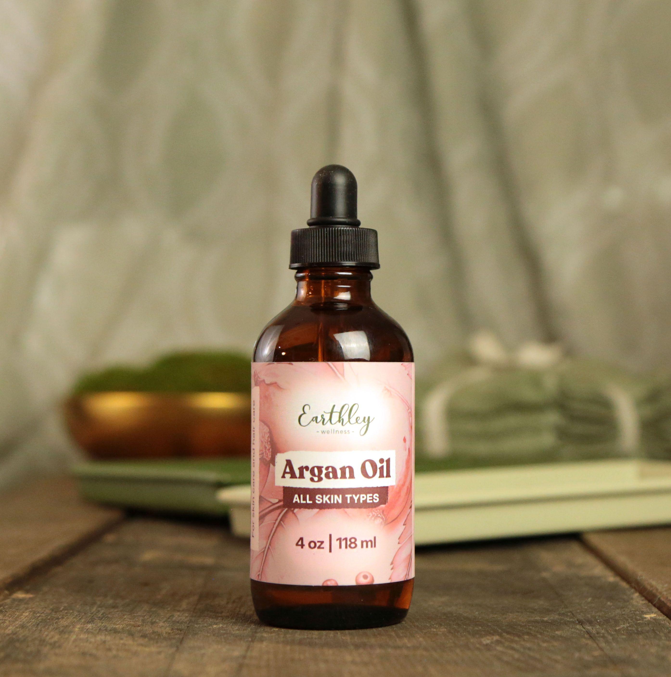 Earthley Argan Oil 4oz amber glass dropper bottle with pink floral label for all skin types on rustic wood surface with spa accessories in background