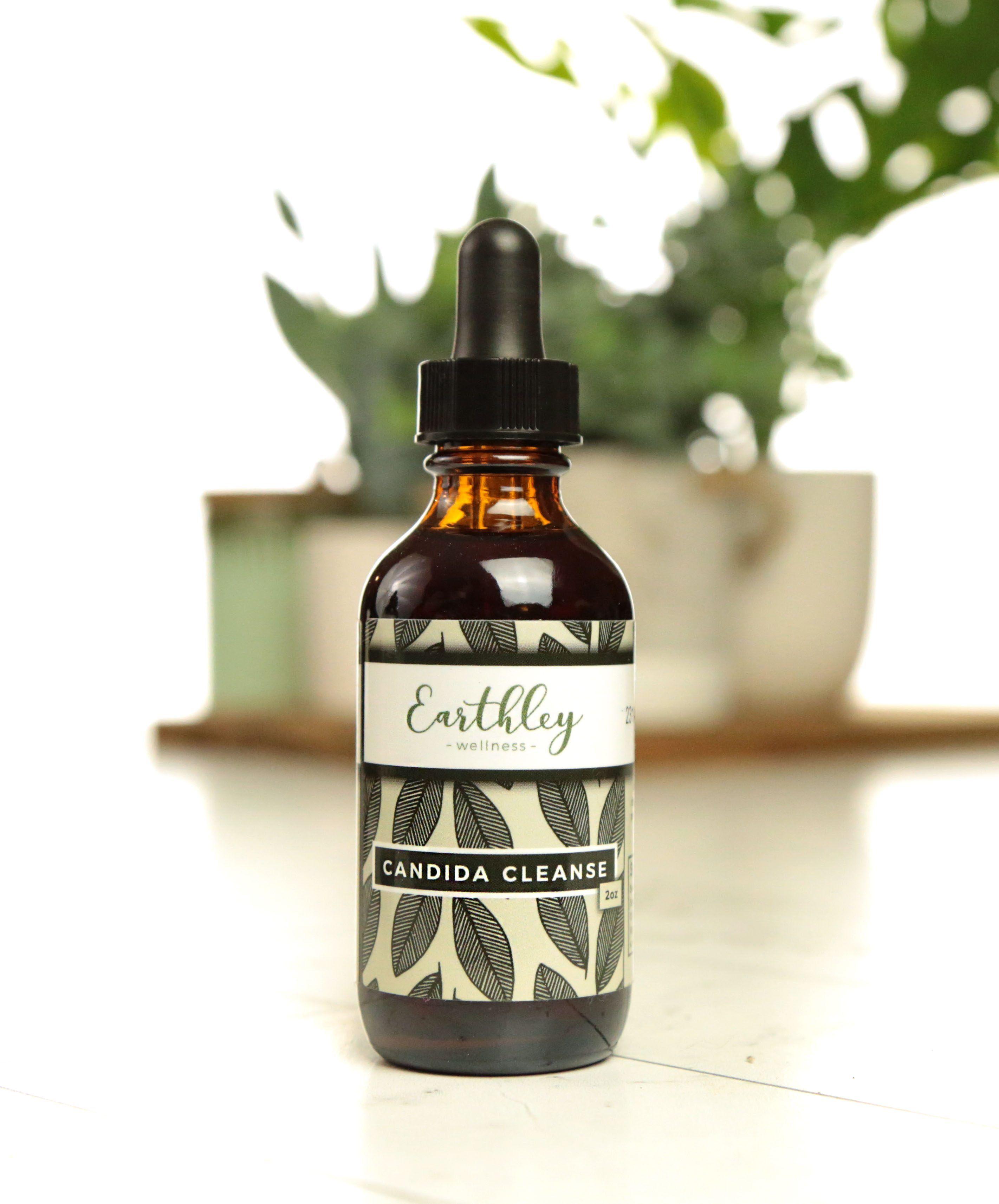 Earthley Candida Cleanse 2oz amber glass dropper bottle with black cap and dark gray olive leaf pattern label on white marble surface with green plants in cream ceramic pot