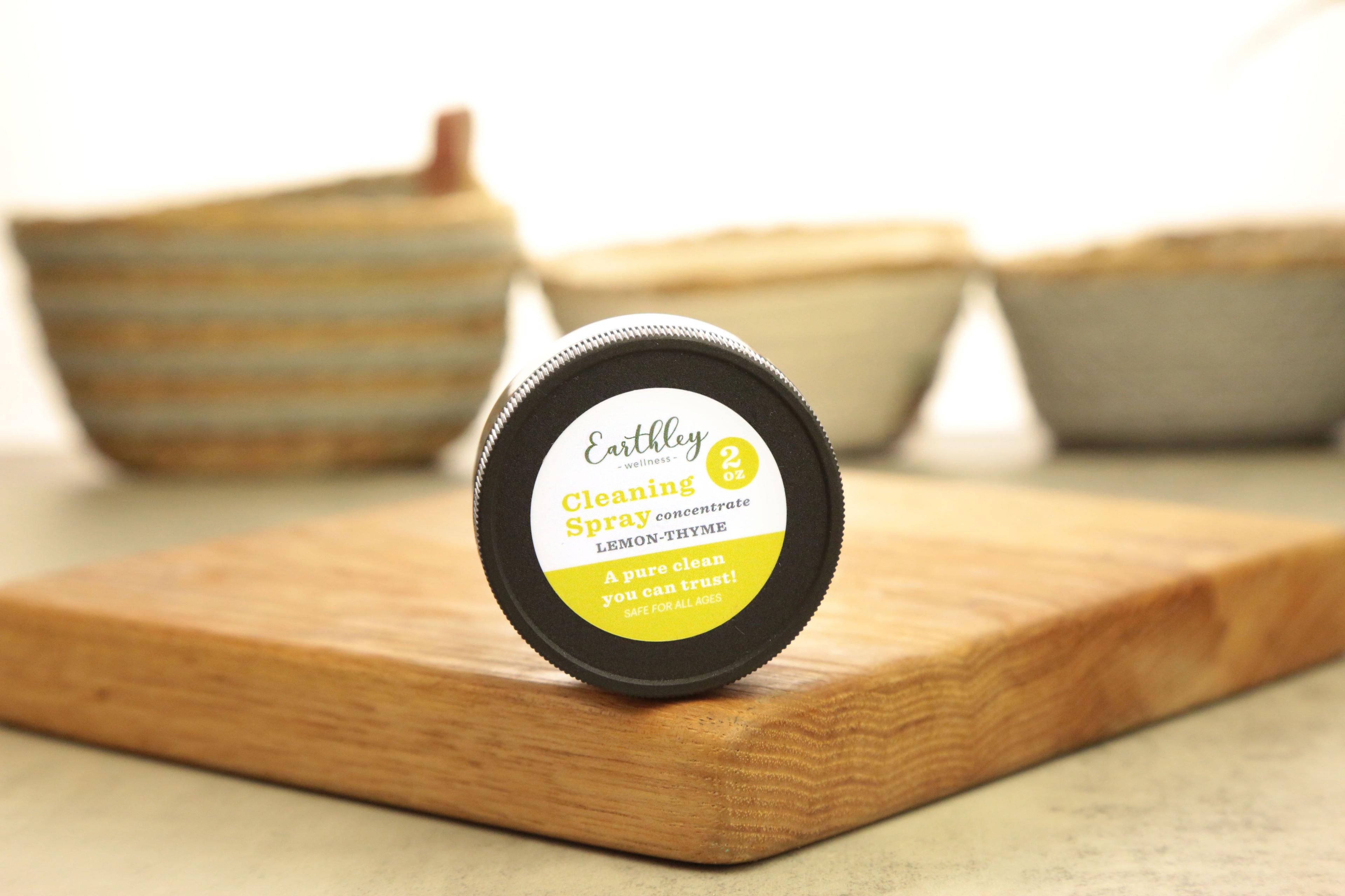 Earthley Cleaning Spray Concentrate Lemon Thyme 2oz black lid with yellow and white label on wooden cutting board with tan and cream ceramic bowls