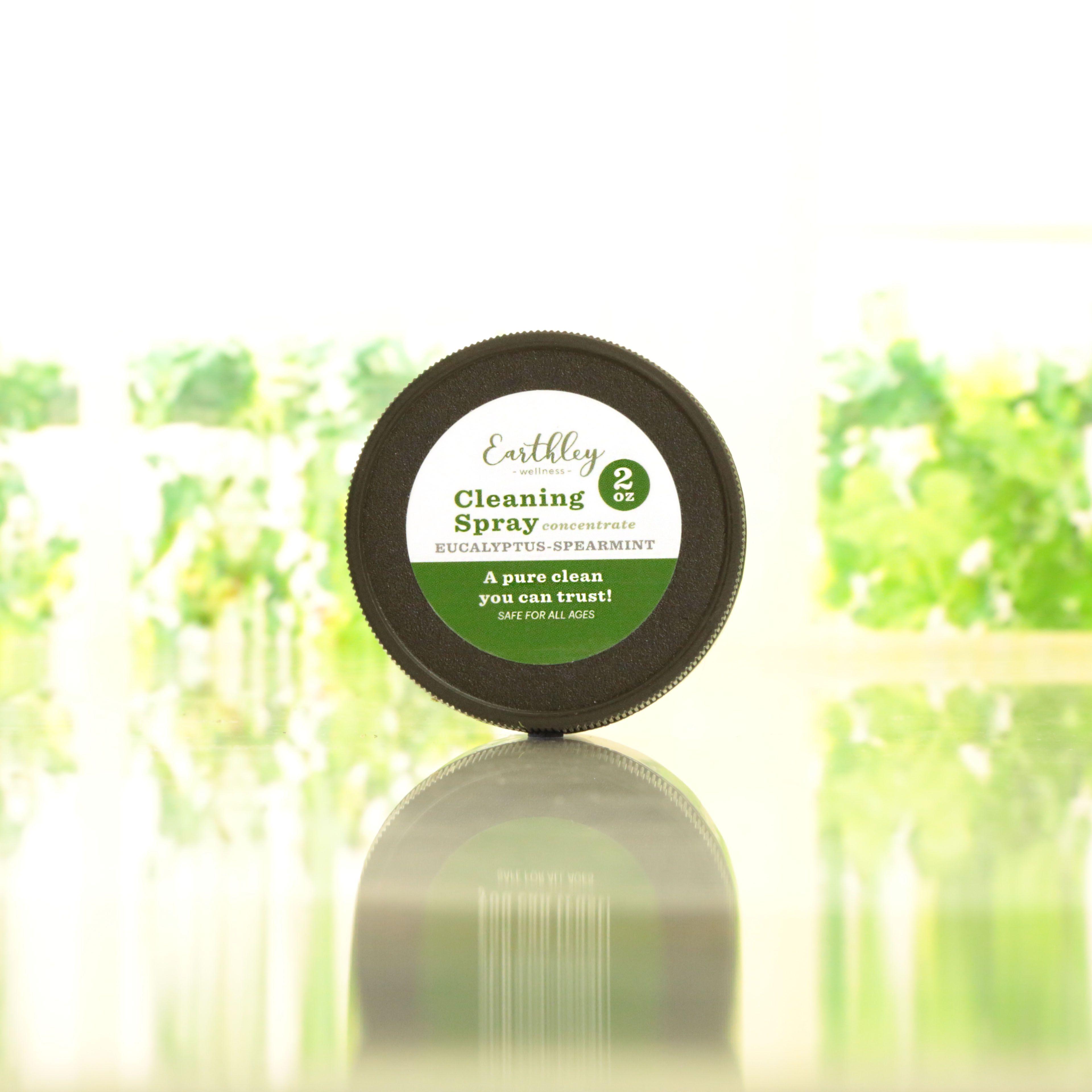 Earthley Cleaning Spray Concentrate Eucalyptus Spearmint 2oz black lid with green and white label on reflective surface with blurred green plants
