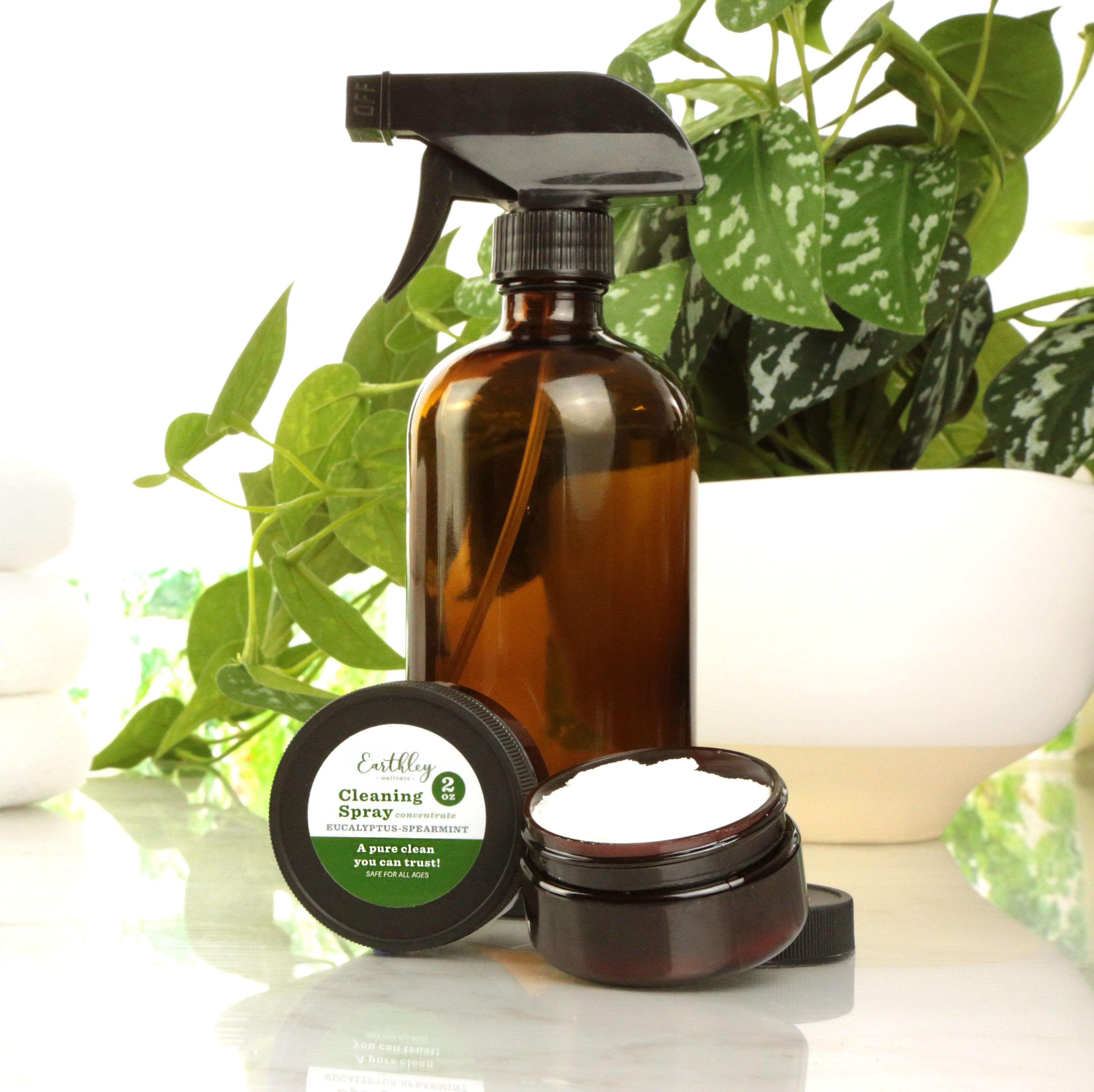 Earthley Cleaning Spray Eucalyptus Spearmint 2oz black lid with amber glass spray bottle and white cleaning paste in amber jar with green label and white pothos plants