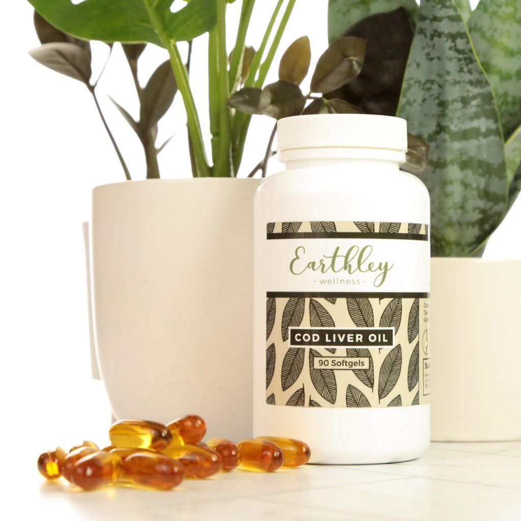 Cod Liver Oil bottle with amber softgels scattered in front and green houseplants