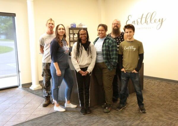 Earthley Yearbook 2023 Support Staff group photo showing employees in casual attire smiling together in warehouse setting with brown boxes