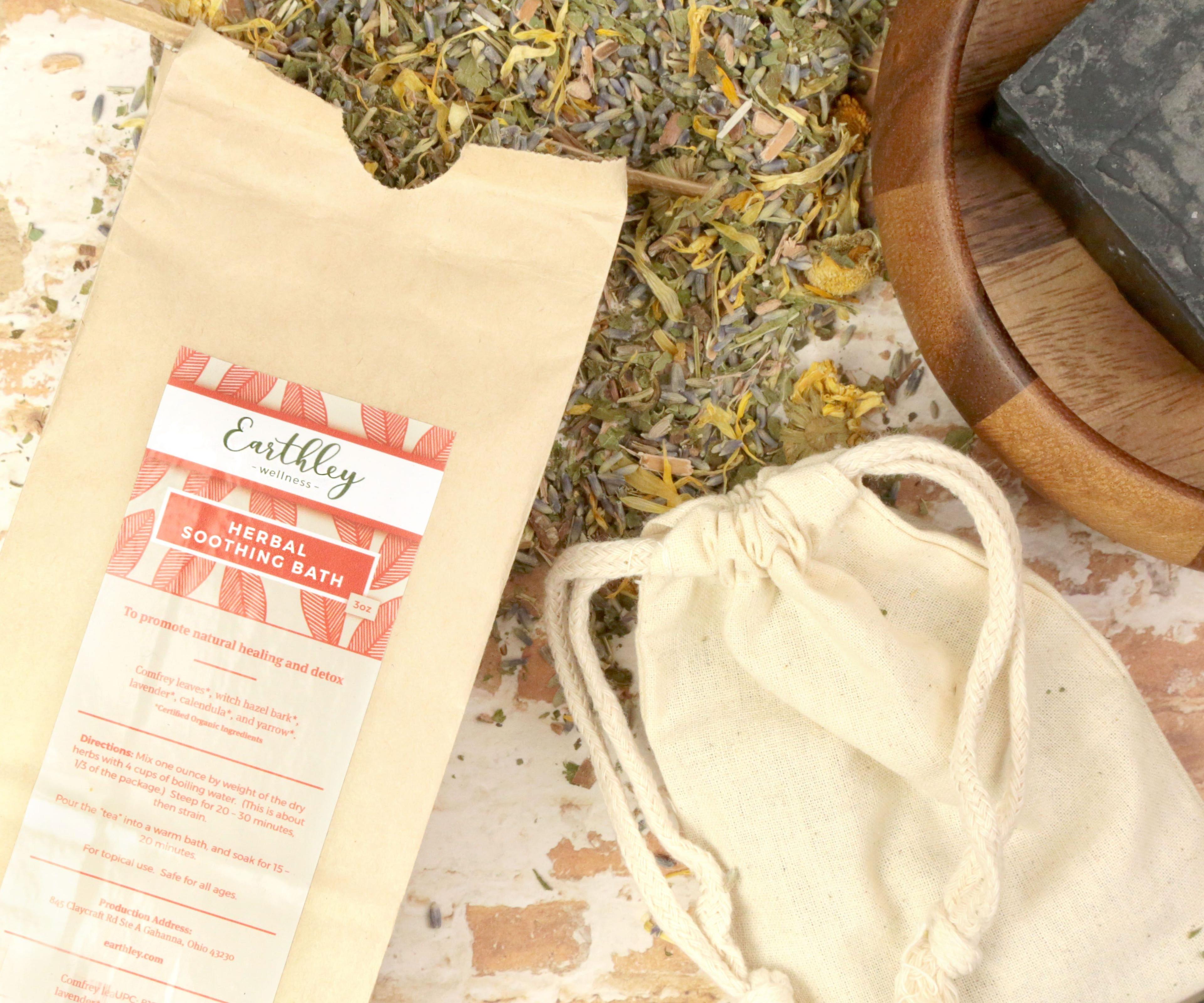 Herbal Soothing Bath in kraft bag with pink leaf label, loose dried herbs, and muslin bag on textured surface
