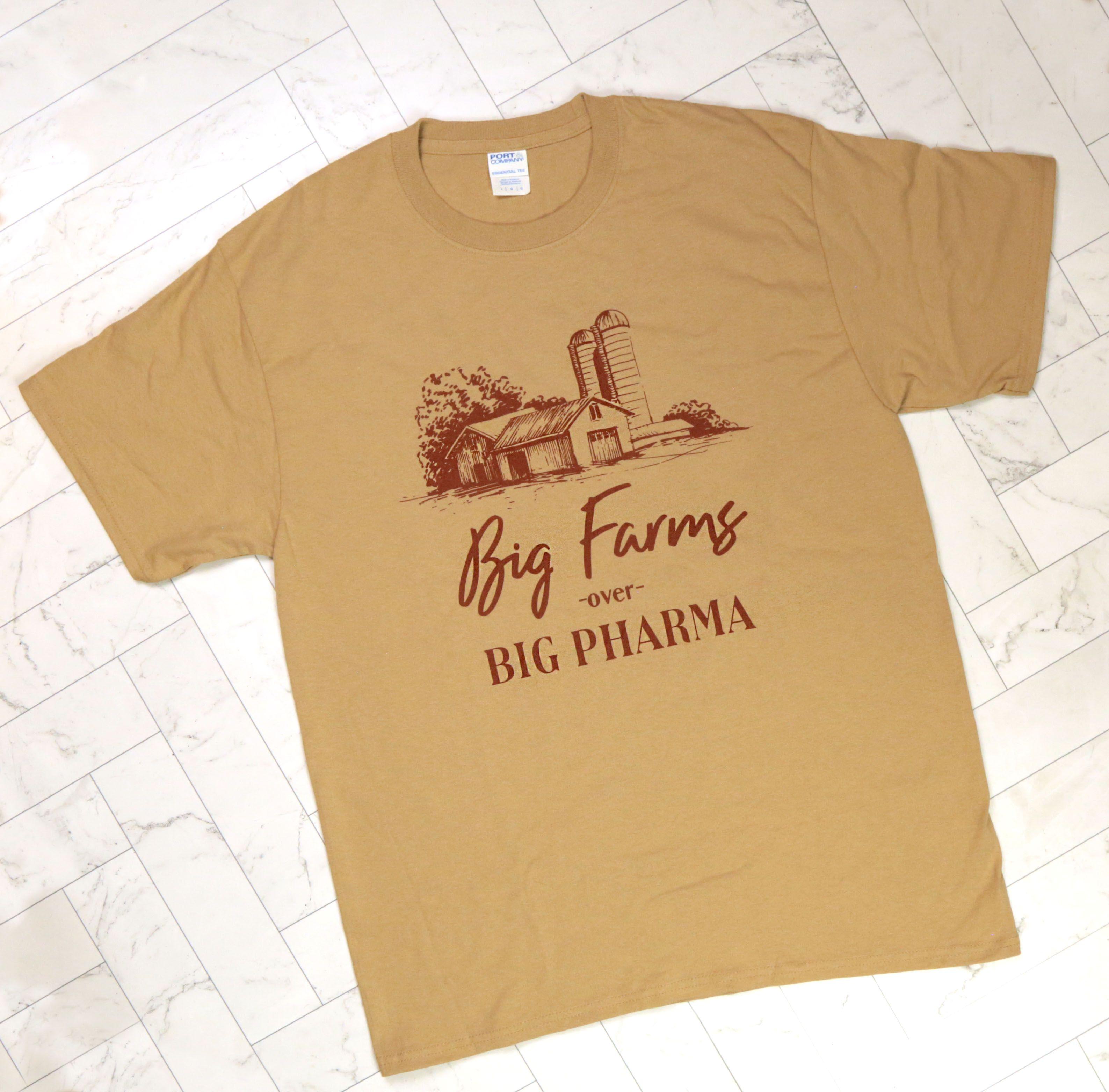 Big Farms over Big Pharma tan gold cotton t-shirt with brown barn and silo illustration on white marble tile background