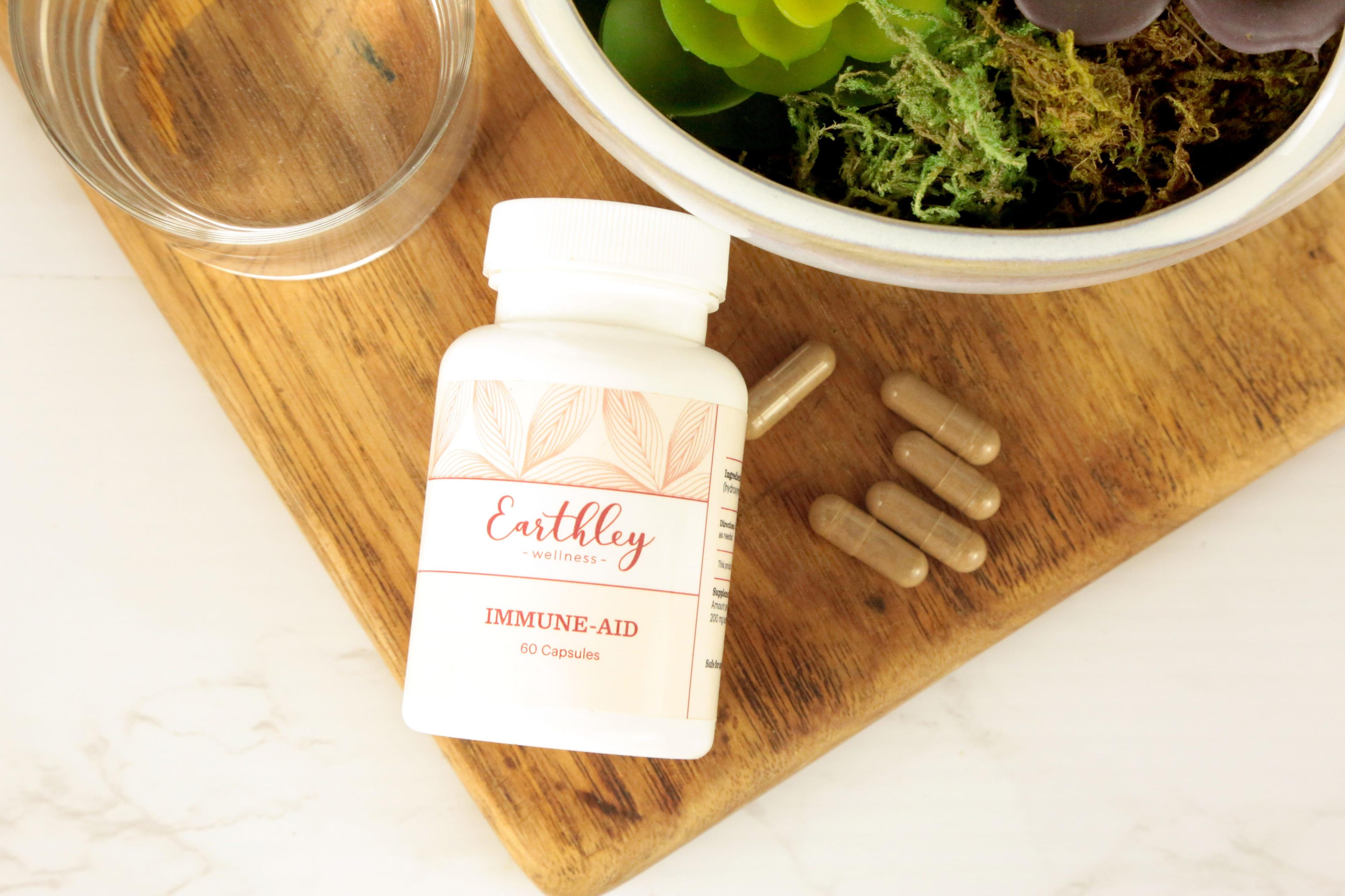 Immune-Aid capsule bottle on wooden cutting board with loose capsules and succulent plant