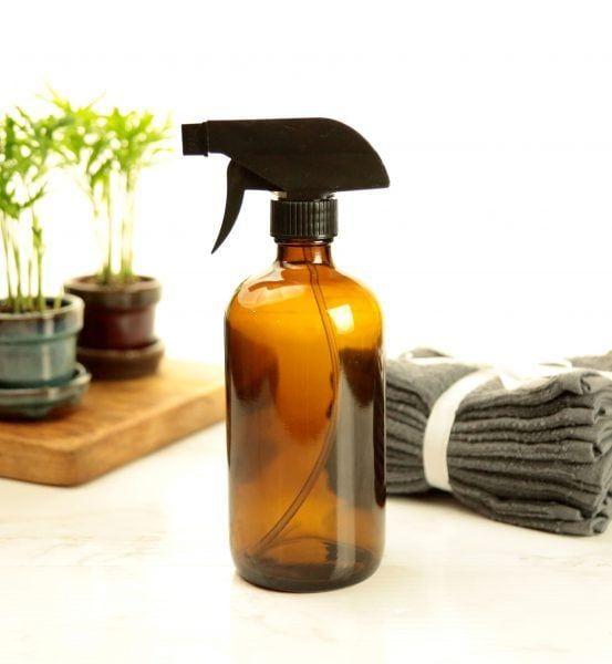Amber glass spray bottle with black trigger sprayer next to gray cleaning cloths