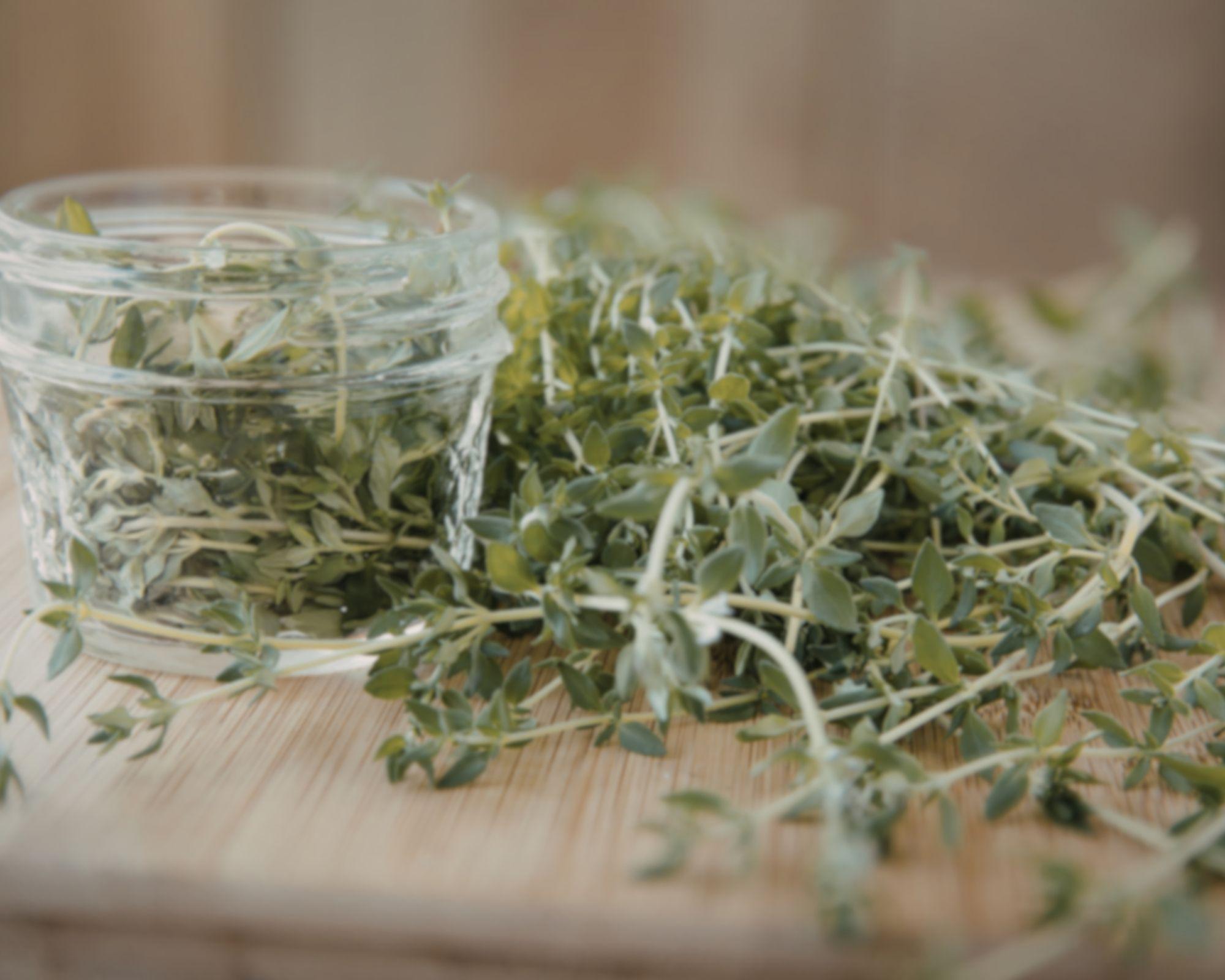 Dried herbs spilling from glass jar onto wooden cutting board for natural remedy preparation