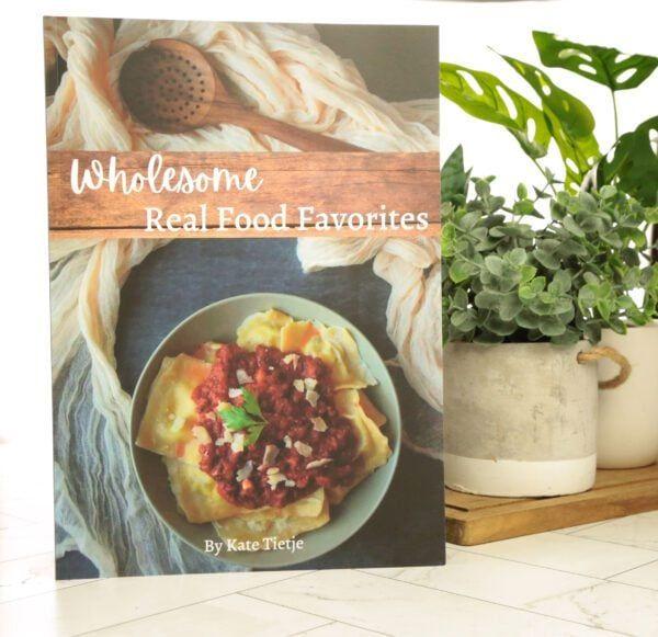 Earthley Wholesome Real Food Favorites cookbook tan kraft box with sage green label showing cooking utensils and fresh ingredients